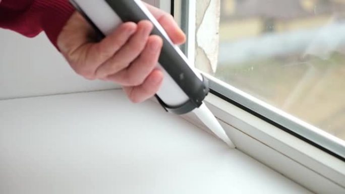一名男子用一根用枪填缝的硅酮密封胶管在窗户和窗台之间的接缝上涂上密封剂。