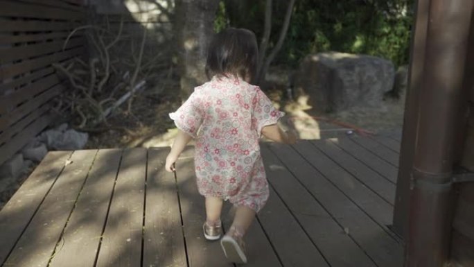 在阳光明媚的日子里，一个穿着和服的日本女婴在她传统木屋的室外走廊上摇摇晃晃地拍摄了慢动作。