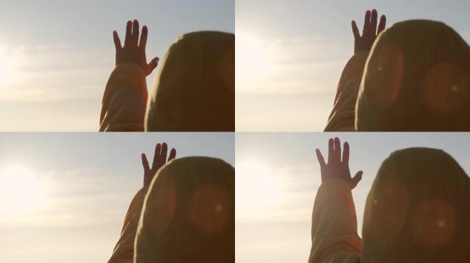 一个幸福的年轻女子的剪影向太阳伸出了手。信仰上帝梦宗教概念。