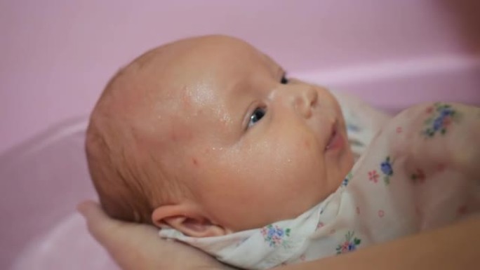 母亲在家用水用粉红色的浴缸洗新生婴儿