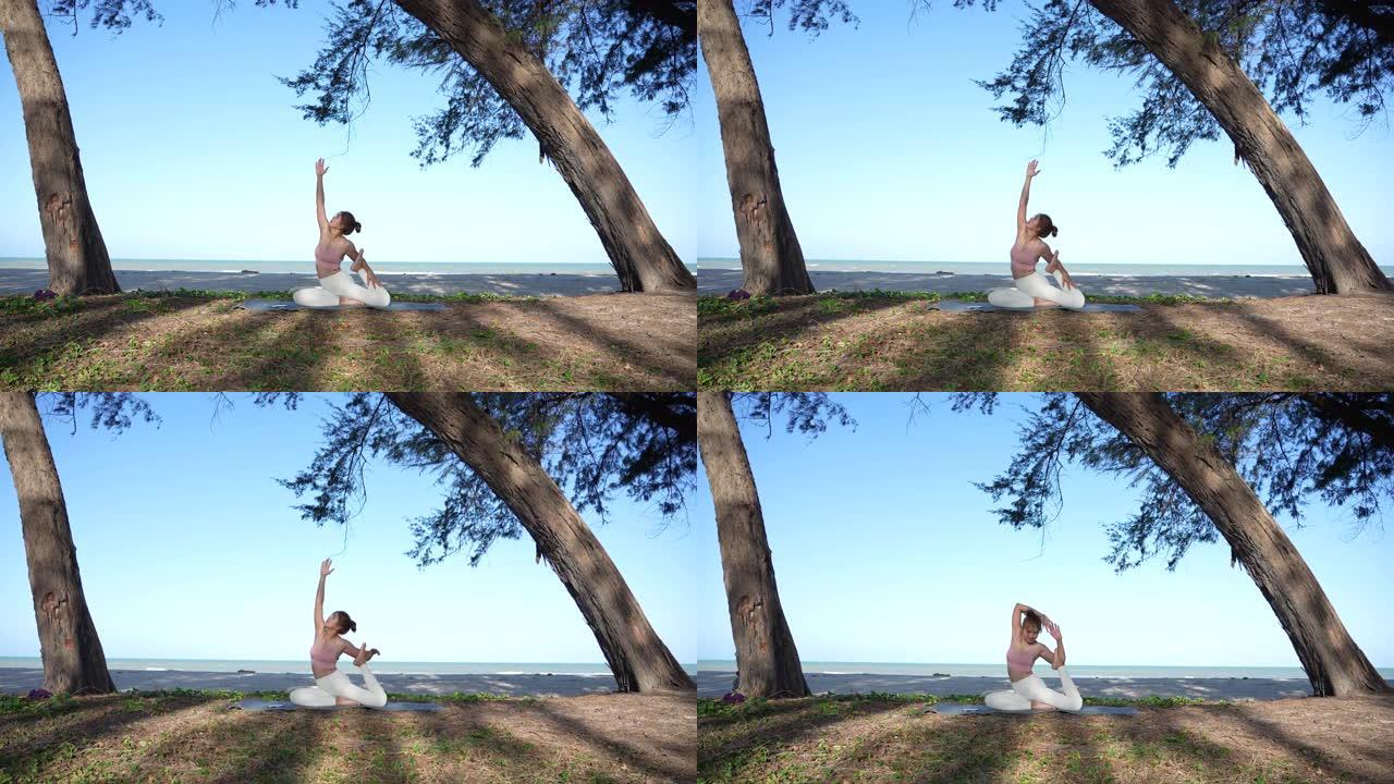 夏日，亚洲女性妈妈在海滩附近的树下练习和做瑜伽