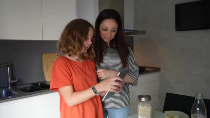 快乐的母女俩在家一起准备早餐，在互联网上阅读烹饪博客，使用数字平板电脑，母亲和青少年制作健康的水果饮