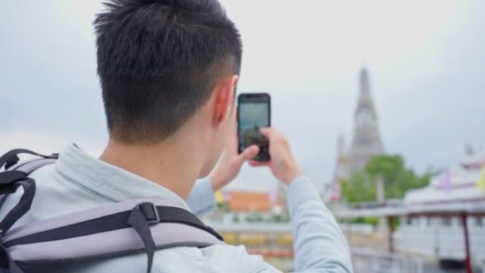 亚洲男子背包客使用手机自拍，在城市拍照。年轻的男性游客独自在街上旅行，在泰国佛寺度假度假旅行中使用手