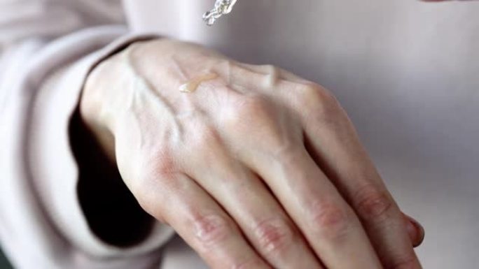 女性手部在手部皮肤上滴精油，用于保湿特写