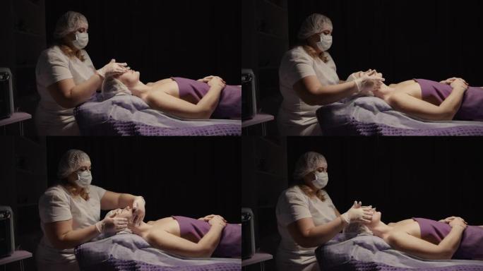 在水疗沙龙接受抗衰老面部按摩的女性放松。健康身体皮肤护理面部美容治疗。黑色背景