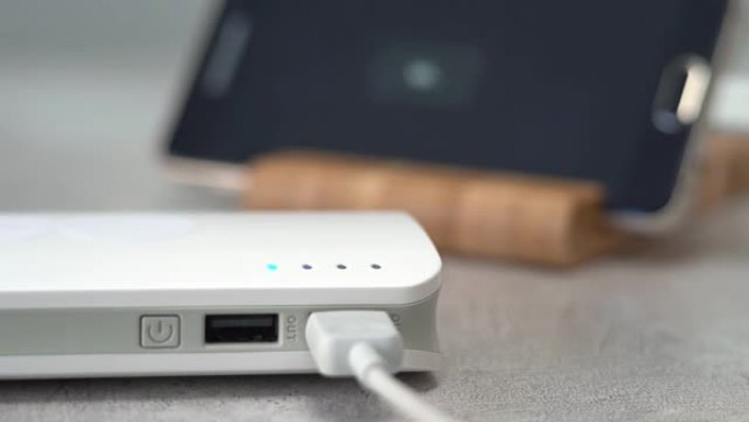 手在手机背景上打开powerbank。外部电池为电子设备充电。闪烁指示器