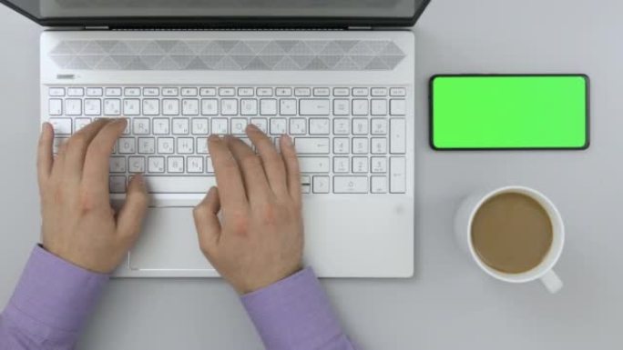 商人在办公桌上的笔记本电脑上打字。绿色模拟屏幕色度键智能手机。学生学习。顶视图工作台创意设计师，自由