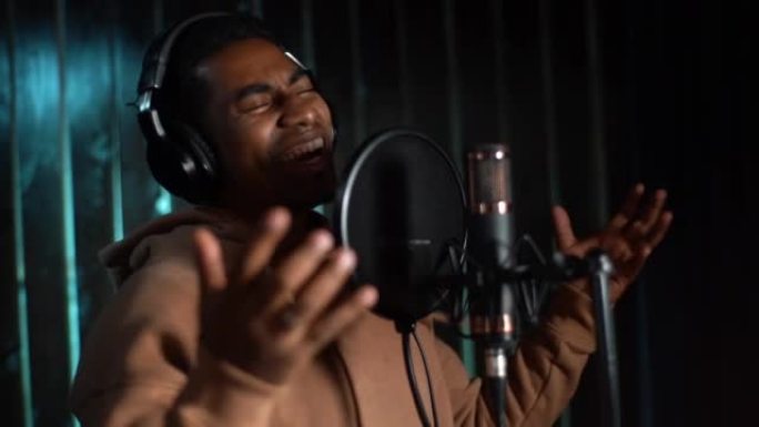 年轻的非裔美国男歌手戴着耳机表演和录制新歌的特写。