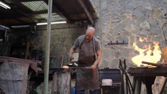 粗暴的中年男人在努力工作。铁匠在砧锤手动锻造熔融金属。一名工人在车间工作。