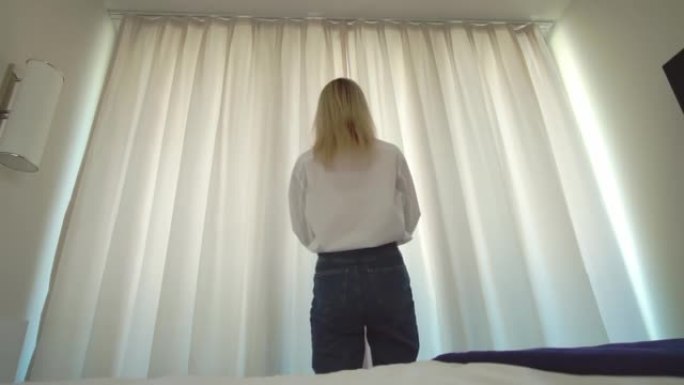 一个穿着白衬衫的女人下床，打开窗户上的窗帘。