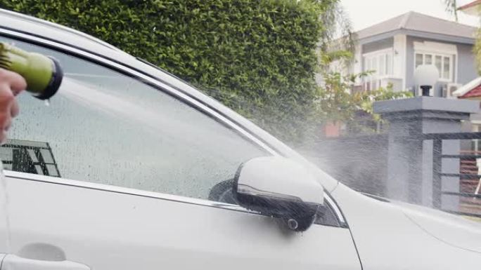 周末，关闭男子喷洒干净的水在家里的白色汽车上清洗干净的污垢