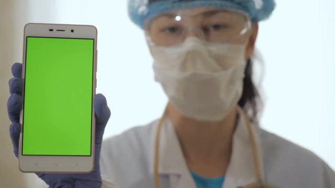 医院机柜中的医疗保健专家使用带模型的智能手机。女医生。戴着防护面罩的高加索女医生拿着手机，柜子里有绿