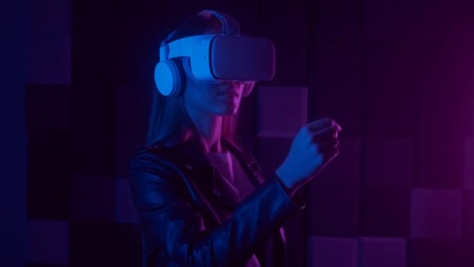 戴着虚拟现实耳机的迷人女人。增强现实。创意女士在室内使用现代3D vr眼镜滑动虚拟屏幕。霓虹灯