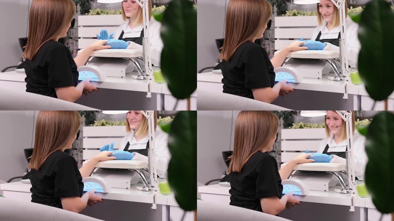 穿着蓝色手套的专业美甲师女子微笑着在美容院与女性客户交谈。指甲油过程中的咨询、检查