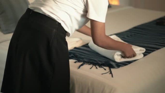 一位年轻的亚洲女服务员穿着制服，拿着一堆干净的折叠毛巾，打算把它们放在酒店房间的换床上