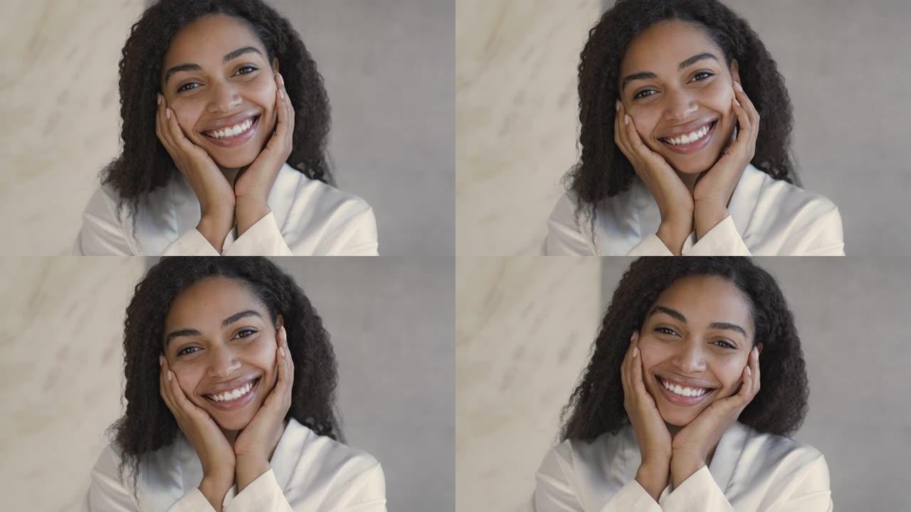 自然美概念。年轻的积极的非洲裔美国女士对着镜头微笑，抚摸着她光滑的脸颊的特写镜头