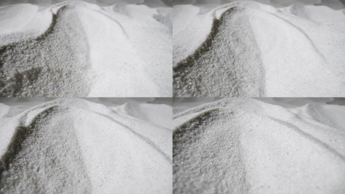 相机在一堆干燥的白沙上平移。在光线下闪闪发光的沙质沙丘的特写镜头。纯天然矿物石英的松散颗粒。慢动作就