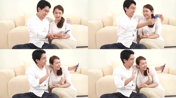 快乐的亚洲夫妇男人和女人在家里的客厅与朋友和家人使用智能手机面对面视频通话。呆在家里检疫，社交距离，