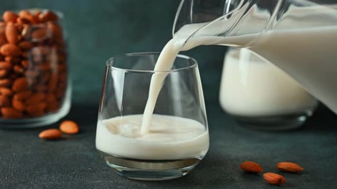 将杏仁奶倒入玻璃杯中。纯素食牛奶。植物性牛奶替代品和无乳糖。替代牛奶。将牛奶倒入玻璃杯中。