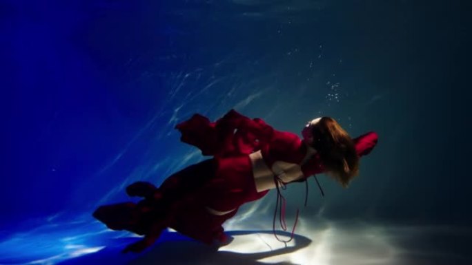 一个年轻女子在水下游泳的神奇水下镜头。红色连衣裙