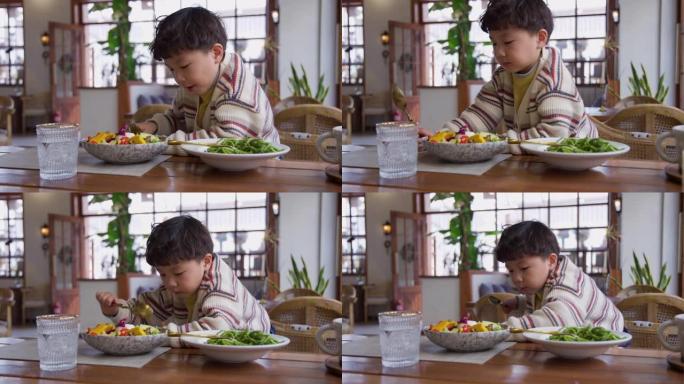 饥饿的小男孩吃蔬菜沙拉