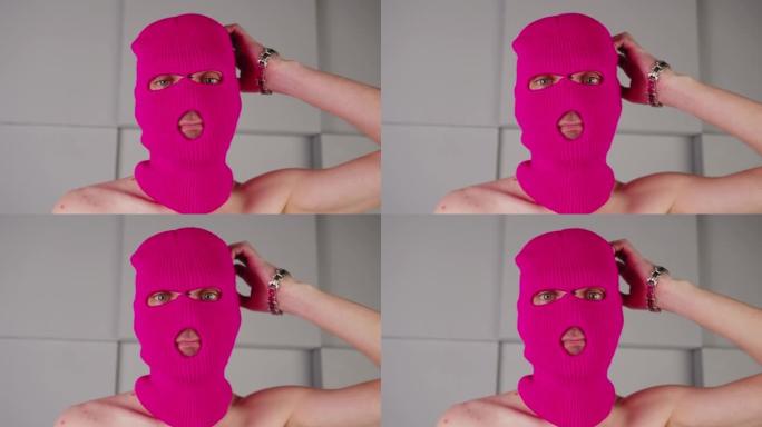 穿着粉红色巴拉克拉法帽的体贴面目全非的人的肖像。戴着面具的流氓看着相机抓挠头