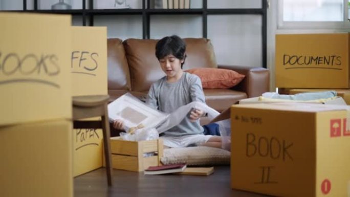 快乐的亚洲儿童男性打开卡盒的肖像，用纸板盒搬到新房子。亚洲儿童青少年微笑着自信和平的家庭搬家理念