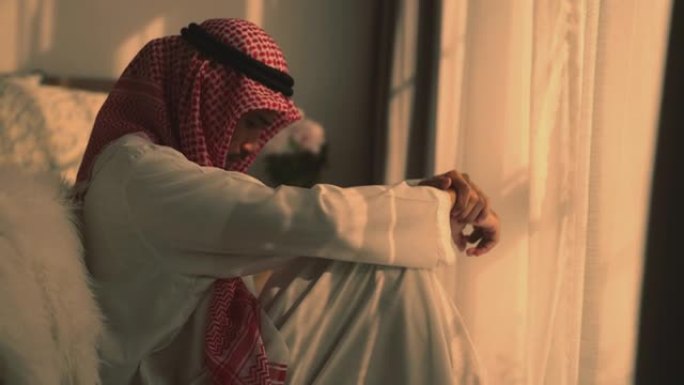 年轻的阿拉伯男子坐在卧室的地板上，表情沮丧地跪下。