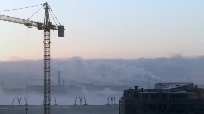 建筑工地的起重机在城市，雾中的工厂和美丽的天空的背景下举起负载