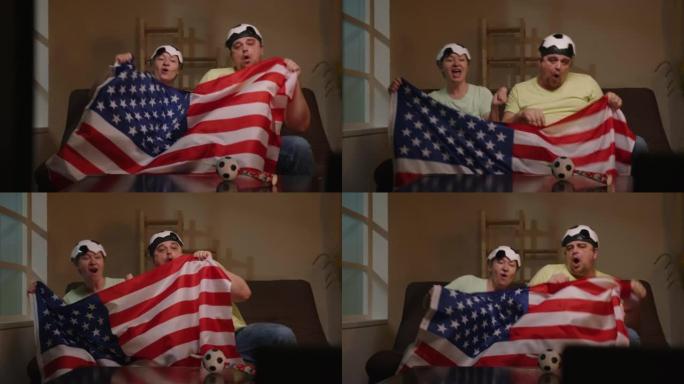 坐在沙发上的足球迷在家里的电视上欢呼挥舞着美国国旗观看比赛