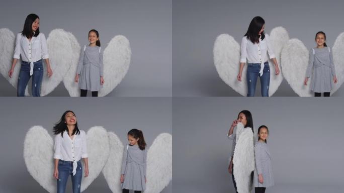 工作室背靠背拍摄微笑的女人和戴着天使翅膀的女孩