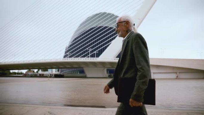 一位务实的老人带着一文件夹在现代大都市周围行走。做生意的成人白发男子