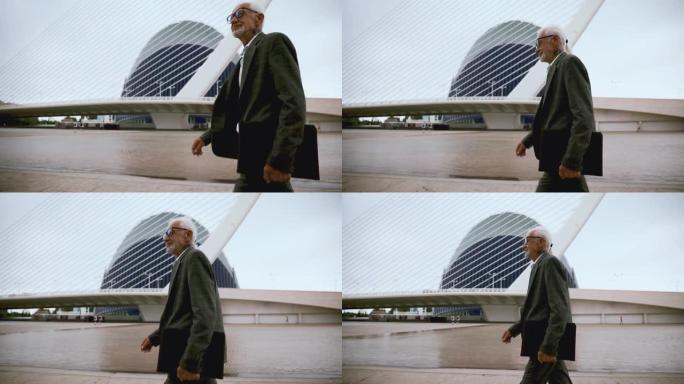 一位务实的老人带着一文件夹在现代大都市周围行走。做生意的成人白发男子
