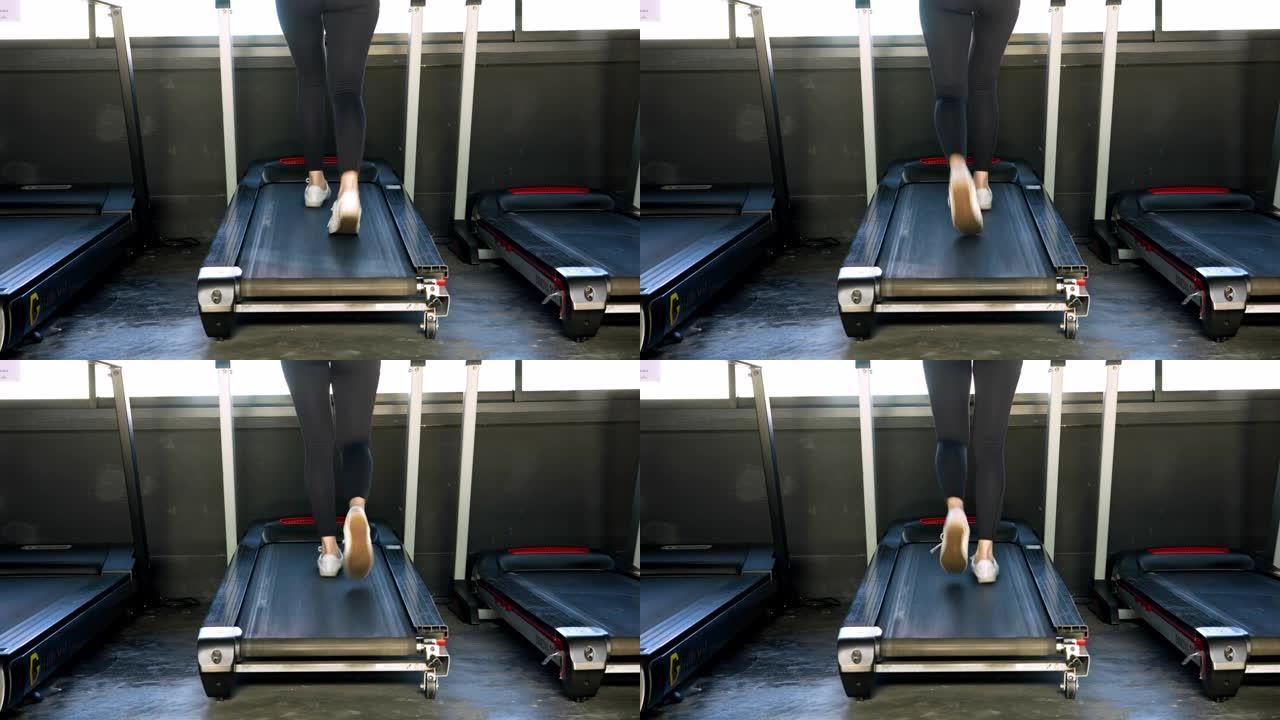 在健身馆的跑步机上跑步的女性运动脚。在跑步机上锻炼的黑色鞋子的后视图。运动俱乐部的低视野运动鞋训练。