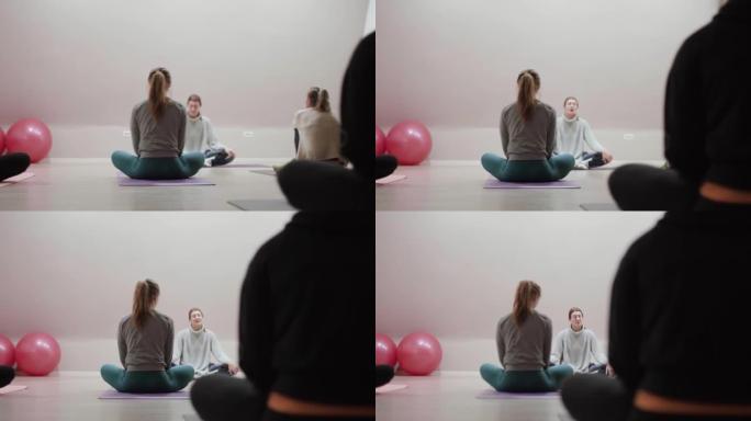 瑜伽教练和学生一起上课。女孩坐着听老师说话 ..