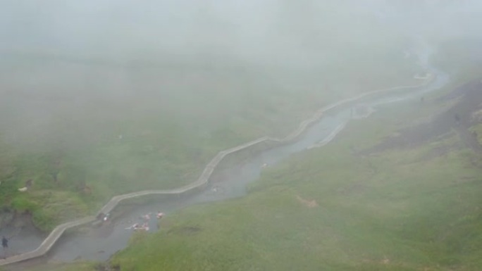 人们在农村流动的热河水中放松。沿着溪流的木板路，雾气从水中升起。冰岛