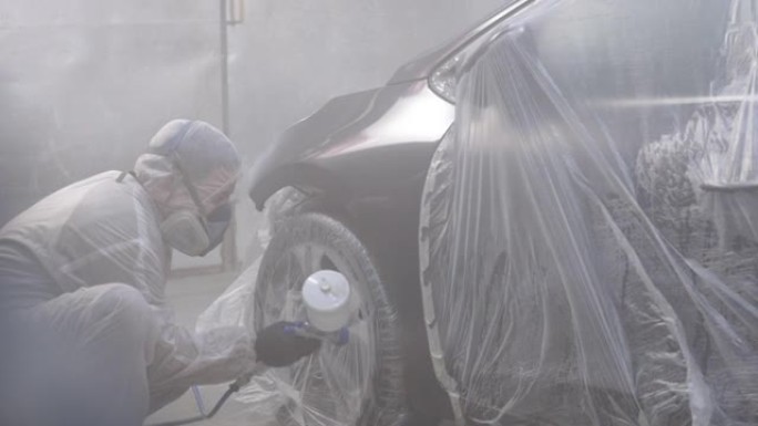 汽车油漆工在特殊的展位上向汽车机翼喷涂黑色油漆，慢动作。在汽车维修车间喷漆车辆零件。汽车制造厂