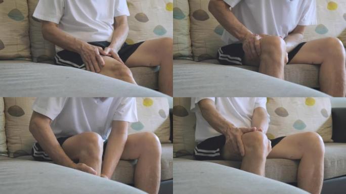 一个亚洲老人抱着膝盖的手的特写。骨头和关节疼痛的人坐在沙发上。一个成熟的男人按摩他痛苦的膝盖。在家受
