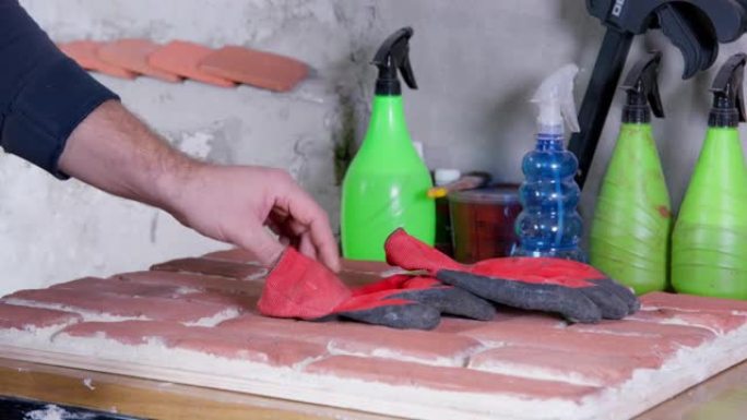 男人戴上橡胶手套，以处理砖头。在车间特写处从事工艺砖坯料制备的专业工人