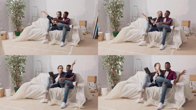 不同国籍的夫妇坐在客厅的沙发上，在装修期间新买的公寓里，情侣在平板电脑上讨论装饰家具墙壁颜色观看项目