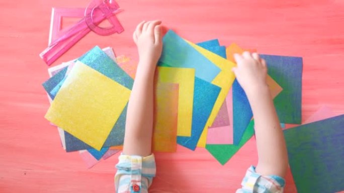 孩子玩彩色压纹纸的手的特写镜头为制作工艺做准备。儿童发展。顶视图
