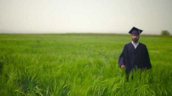 男人走在绿色的田野里。脱下毕业服装，向空中扔帽子。