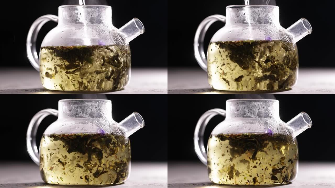 在深色背景下的玻璃透明茶壶中酿造绿茶的过程。将热水倒入带茶叶的水壶中。