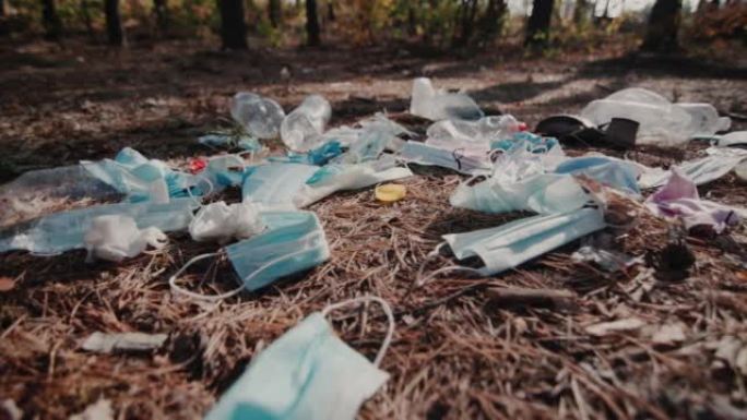 宽镜头拍摄: 医用口罩和塑料碎片躺在森林中的地面上