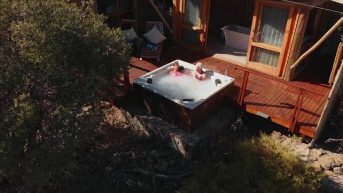高级夫妇在野生动物园小屋外的热水浴缸里放松