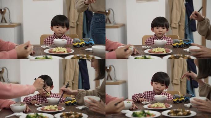 无聊的亚洲男婴与玩具车的选择性焦点看着他母亲在餐桌上提供的菜。儿童饮食习惯与营养观念
