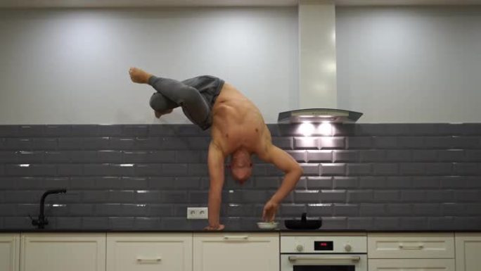 男子在厨房里练习倒立和烹饪食物。瑜伽、健康和健康生活方式的概念