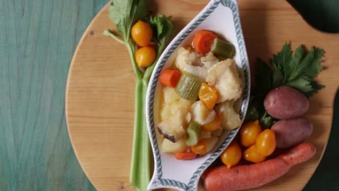 煮鳕鱼配土豆、芹菜和胡萝卜。准备烹饪的盘子的特写镜头，在绿色的木制背景上