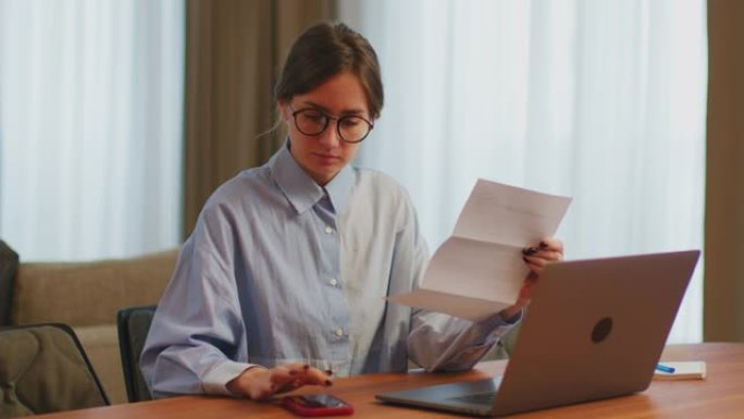 女会计簿记员使用电话和笔记本电脑计算账单或税款，在办公桌上管理财务费用