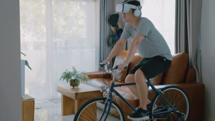 一名亚洲男子在新型冠状病毒肺炎禁闭期间用VR护目镜在家骑自行车。